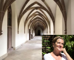Ein steinerner Korridor mit gewölbten Decken und gotischer Architektur; in der Ecke sitzt eine Frau in einem weißen Oberteil im Freien und lächelt nachdenklich über das Grün im Hintergrund - vielleicht denkt sie über einen Workshop zur Stimmbildung nach.